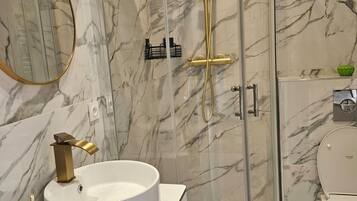 Un baño moderno con cabina de ducha de vidrio curvo, un lavabo redondo con grifo dorado y un inodoro.