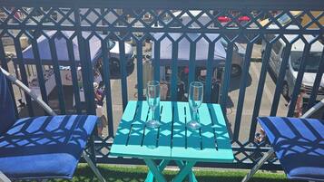Un balcon avec une table et des chaises, donnant sur un parking où sont installées des tentes et garés des véhicules.