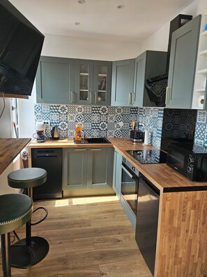 A modern kitchen with grey cabinets, a wooden countertop, and patterned backsplash tiles. - Renovated and well equipped apartment in the heart of Mers and close to the beach. (Mers-les-Bains)