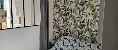 A bedroom with a bed, a window with curtains, a wall with a leaf pattern, and a hanging light fixture.