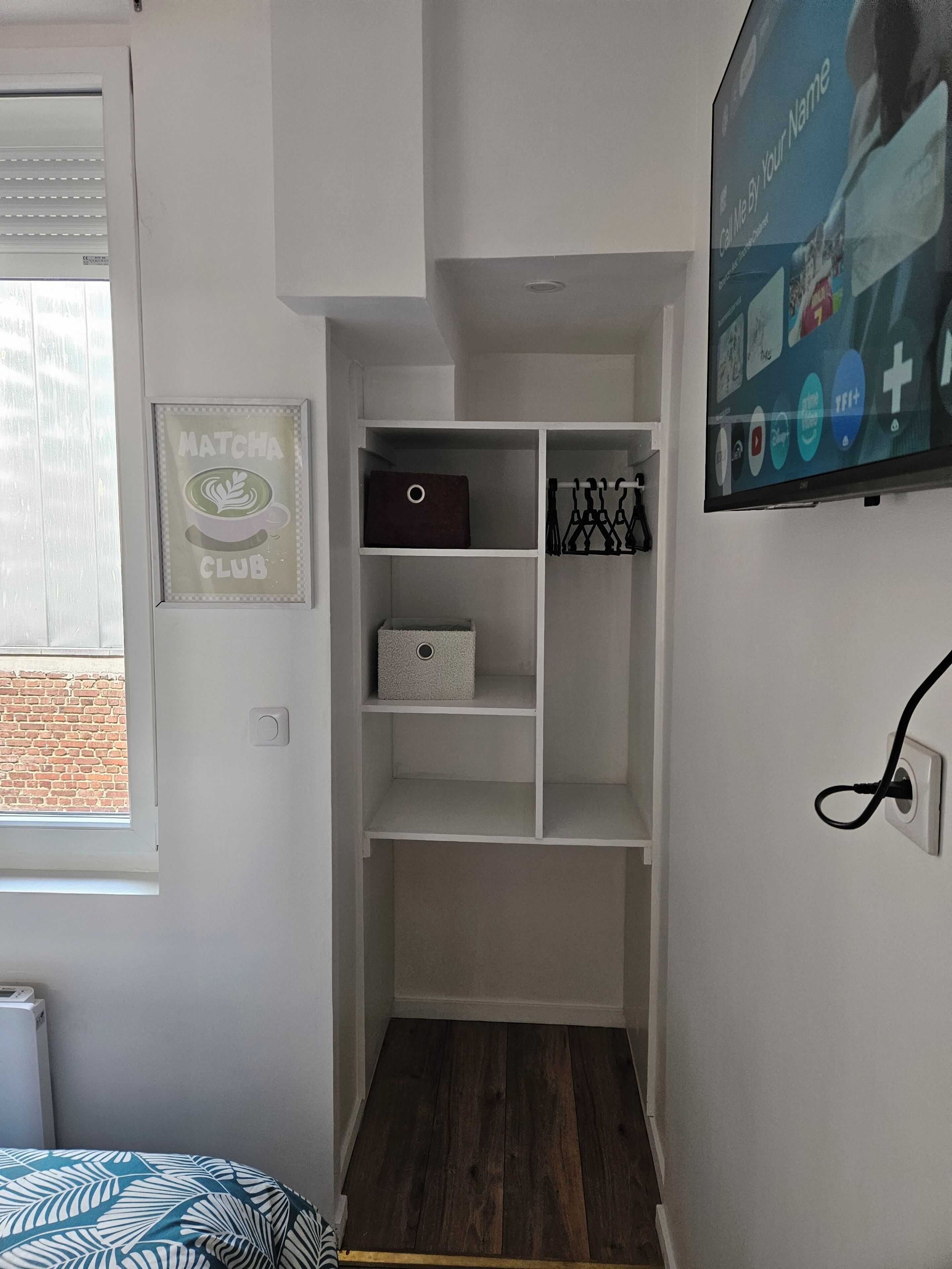 Ein Zimmer mit Einbauschrank, einem gerahmten Bild an der Wand und einem wandmontierten Fernseher.
