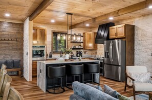 A modern kitchen with wooden cabinets, a stainless steel refrigerator, and a bar area with stools. - Luxe Indoor Pool | Sauna | Theater | Sleeps 16 (Sevierville)