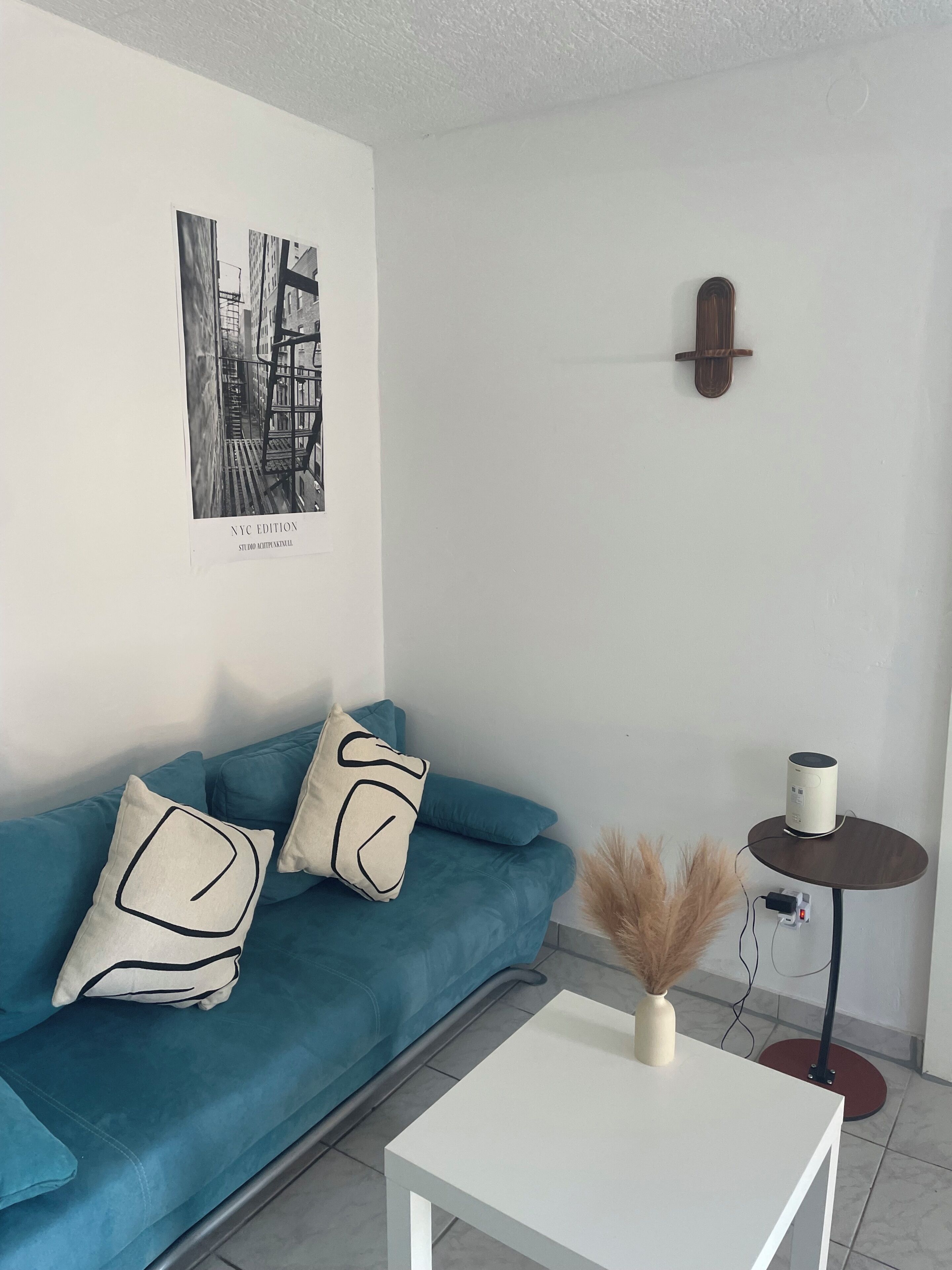 Ein modernes Wohnzimmer mit einem türkisfarbenen Sofa, einem weißen Couchtisch, einer Wandleuchte und einem schwarz-weißen Foto im Bilderrahmen.