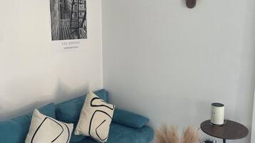 Ein modernes Wohnzimmer mit einem türkisfarbenen Sofa, einem weißen Couchtisch, einer Wandleuchte und einem schwarz-weißen Foto im Bilderrahmen.