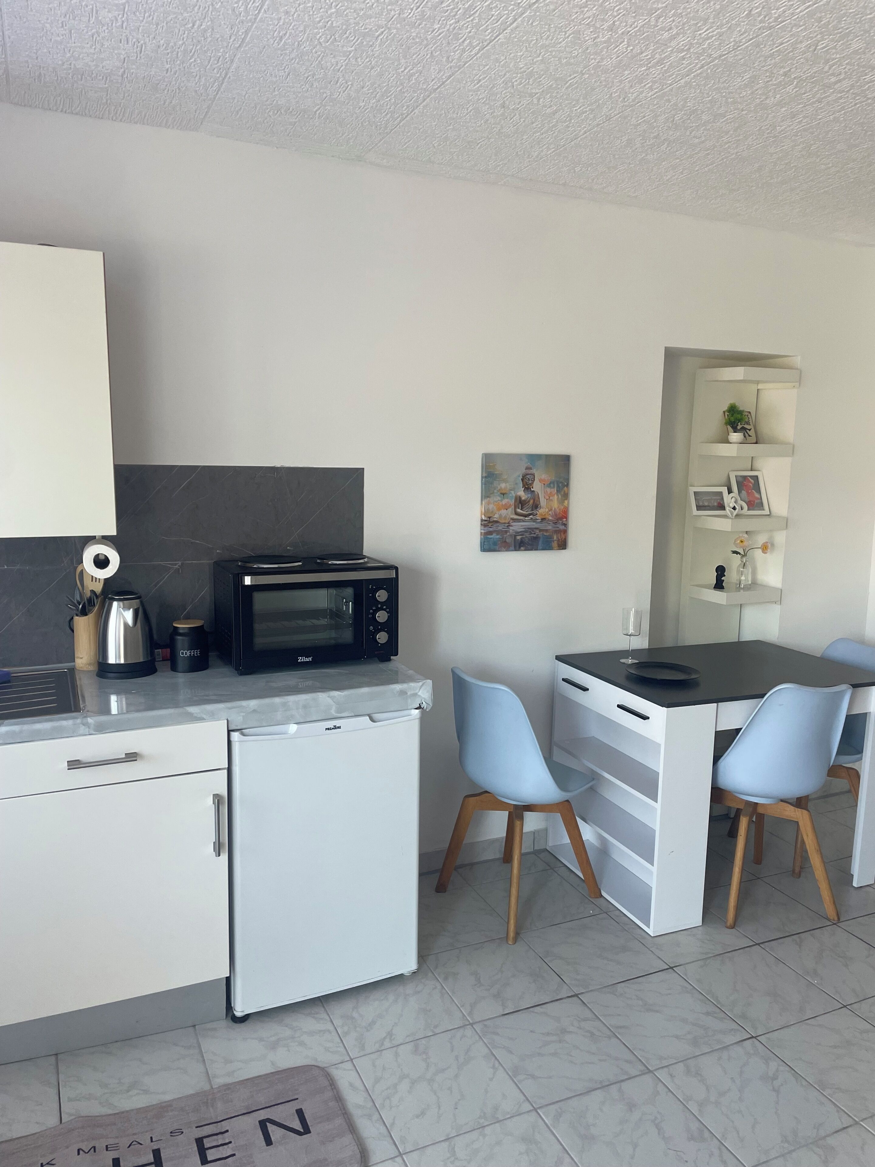 A compact kitchen with a microwave, coffee maker, and a small refrigerator. There is a dining area with a table and two chairs.
