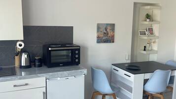 Eine kompakte Küche mit Mikrowelle, Kaffeemaschine und kleinem Kühlschrank. Ein Essbereich mit Tisch und zwei Stühlen vorhanden.
