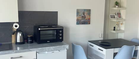 A compact kitchen with a microwave, coffee maker, and a small refrigerator. There is a dining area with a table and two chairs.
