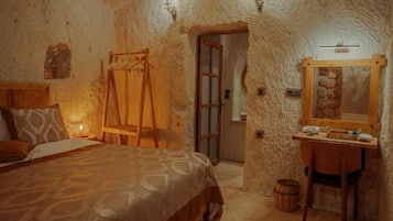 A rustic room with a bed, a wooden desk, a mirror, and a door.