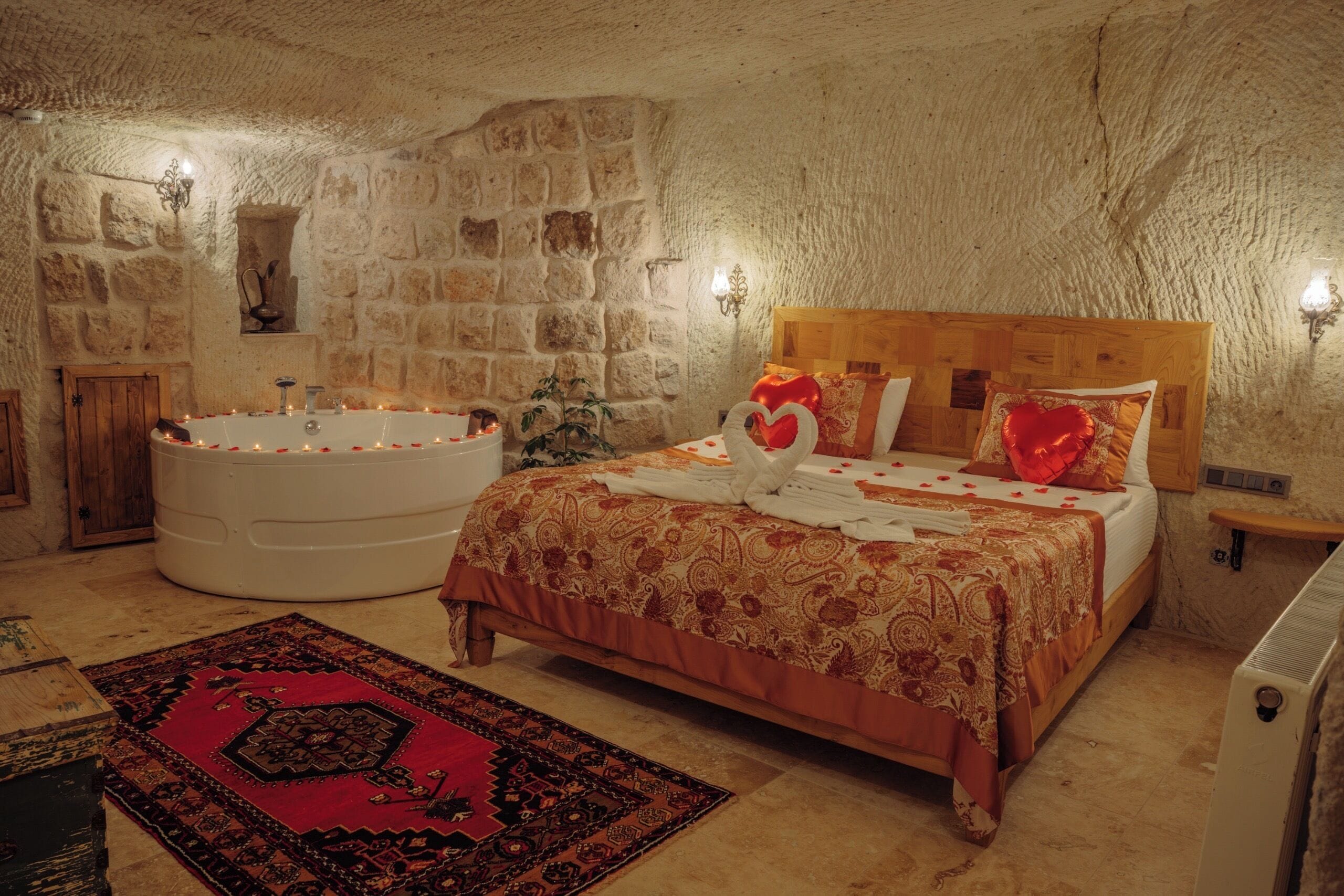 A bedroom with a stone wall, a large bathtub, a wooden bed, and a red patterned rug.