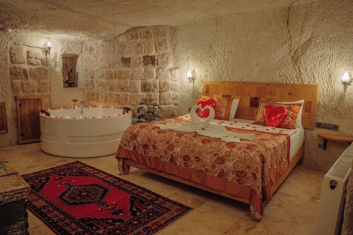 A bedroom with a stone wall, a large bathtub, a wooden bed, and a red patterned rug.