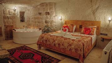 A bedroom with a stone wall, a large bathtub, a wooden bed, and a red patterned rug.
