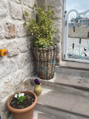 Um muro de pedra com um vaso de cestaria, uma planta em vaso com flores brancas e um detector de incêndio amarelo.
