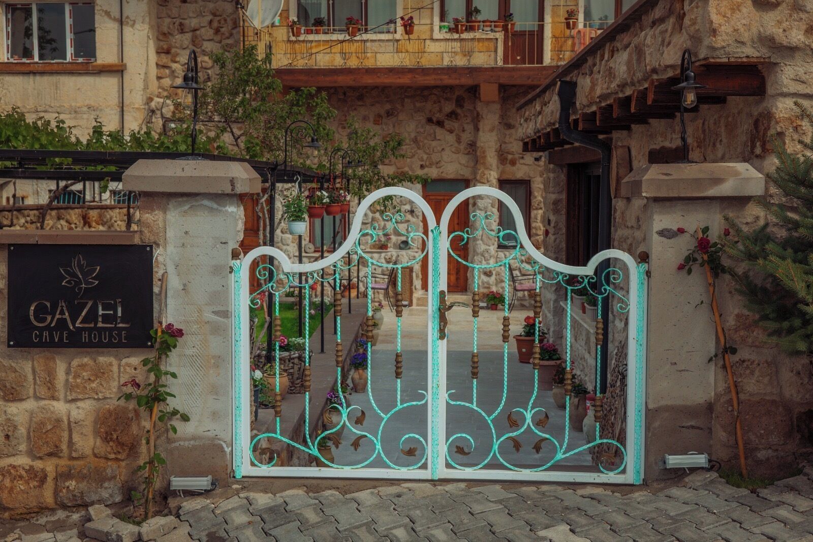 Una reja de hierro forjado con un letrero que dice 'GAZEL CAVE HOUSE' frente a un edificio de piedra con balcones.