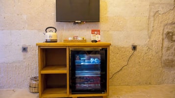 A small wooden cabinet with a television mounted above it, a kettle, and a small refrigerator with a glass door.