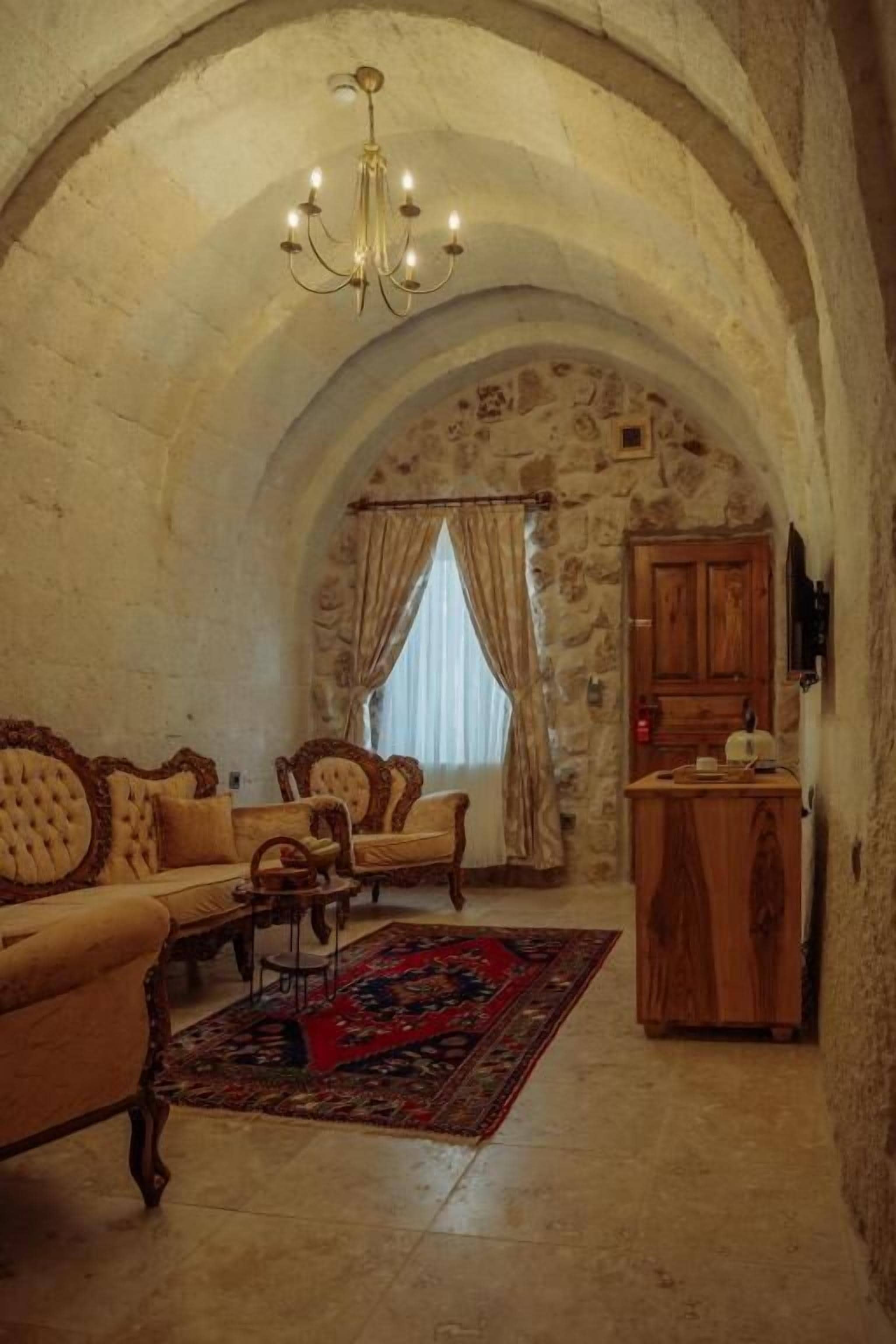 A room with a stone archway, a chandelier, a sofa, a wooden cabinet, and a patterned rug.