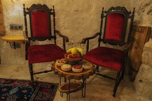 Dos sillas ornamentadas con tapicería roja, una pequeña mesa de madera con fruteros y platos, y una alfombra estampada en el suelo.