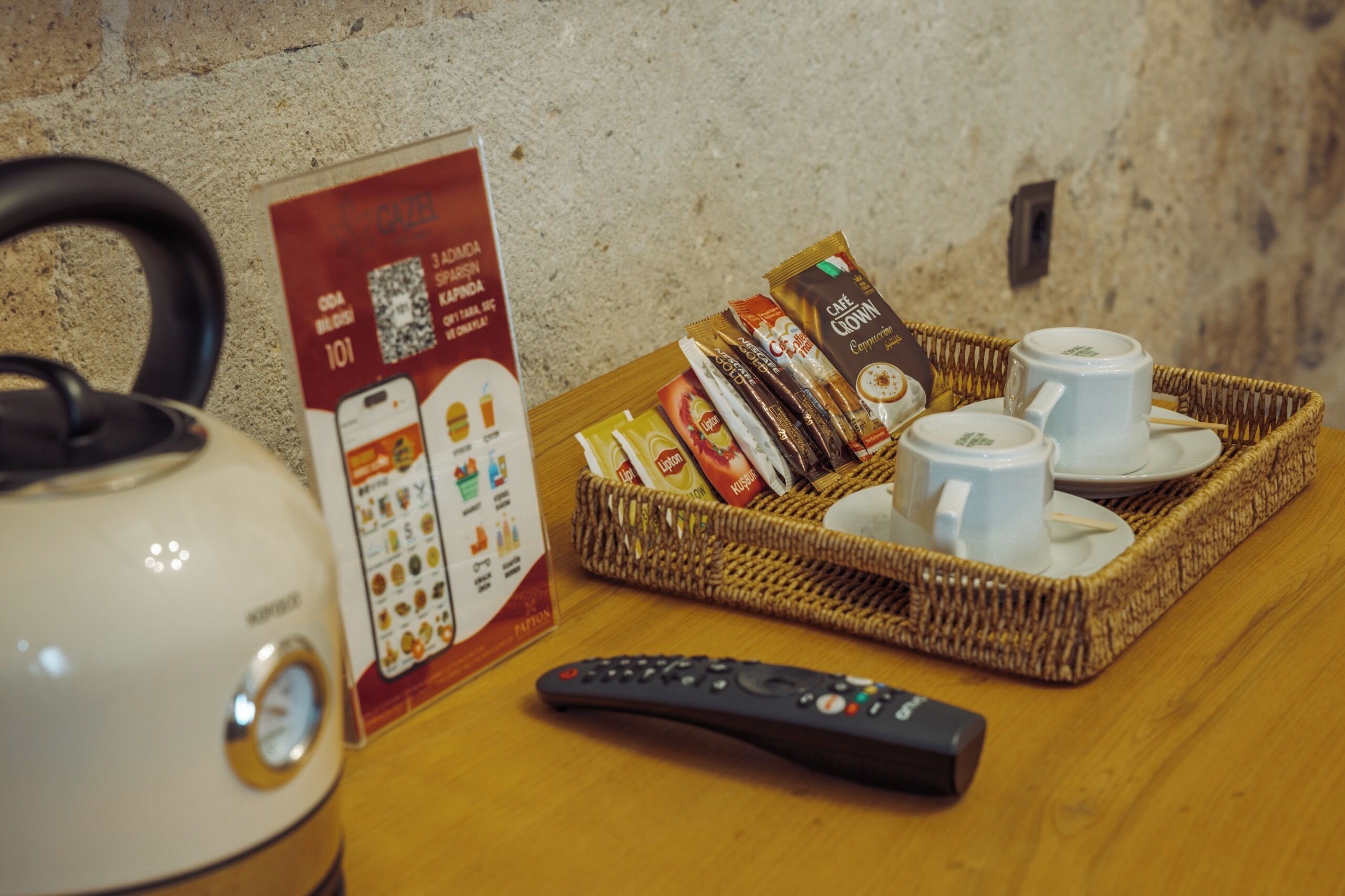 Une bouilloire, une télécommande, un plateau avec des sachets de café et un menu sur une table en bois.