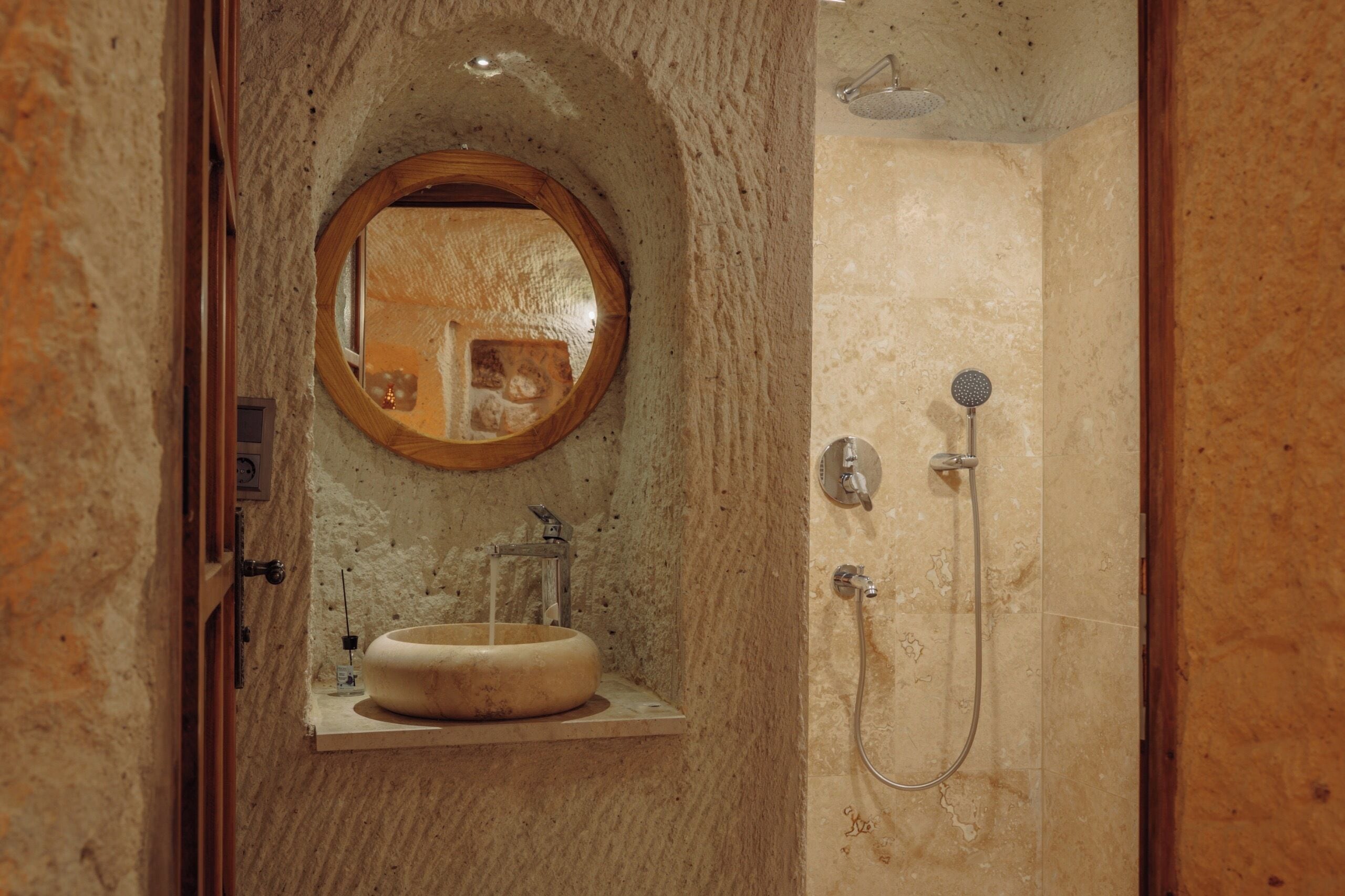 A bathroom with a stone wall, a wooden-framed mirror, a sink, and a shower with a handheld showerhead.