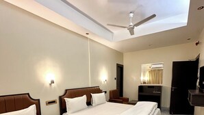 Habitación de hotel con dos camas, ventilador de techo, televisor de pantalla plana y espejo.