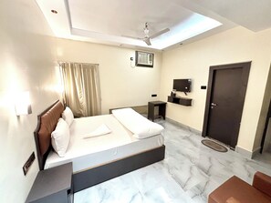 Habitación de hotel con cama, escritorio, ventilador de techo, televisión y puerta.