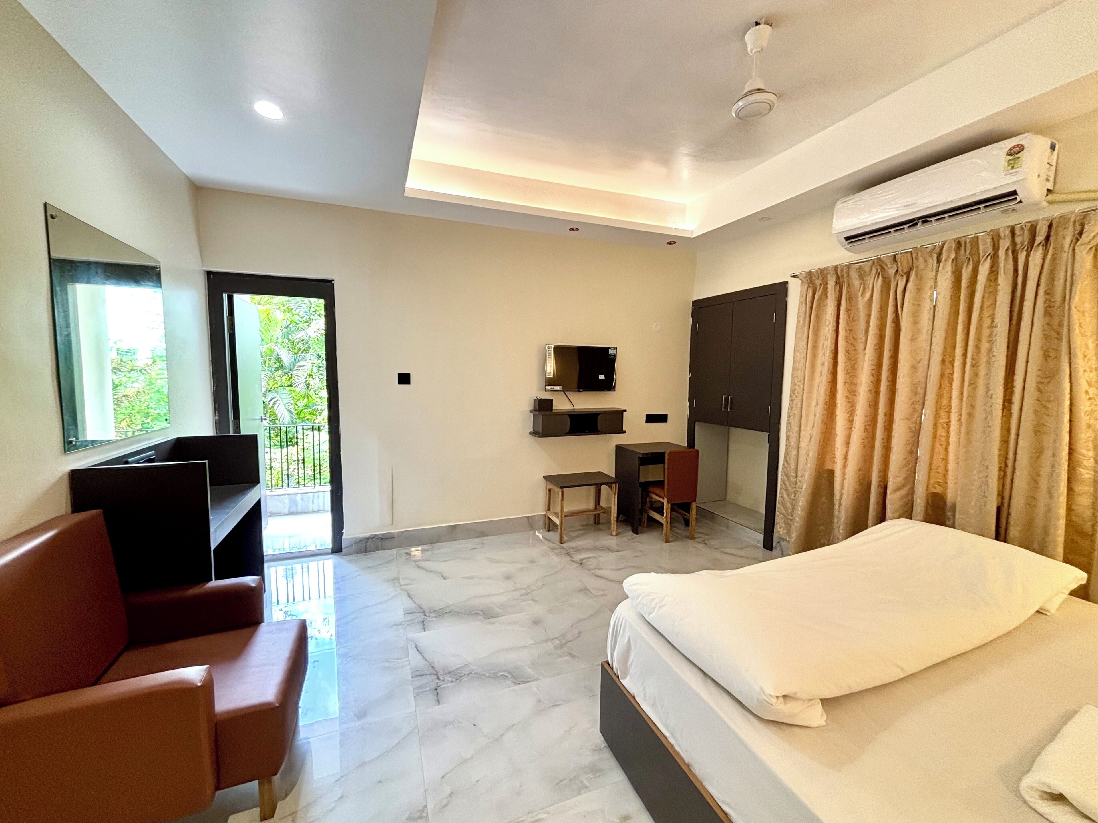 A hotel room with a bed, a desk, a chair, a television, and an air conditioning unit.