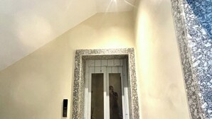 Una habitación con una puerta, un ventanal pequeño y una lámpara en el techo.