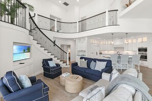 A spacious living area with a curved staircase, a kitchen with white cabinets, and a dining area with a table and chairs. - Waterfront Marco Island Home w/ Pool, Spa & Kayaks (Marco Island)