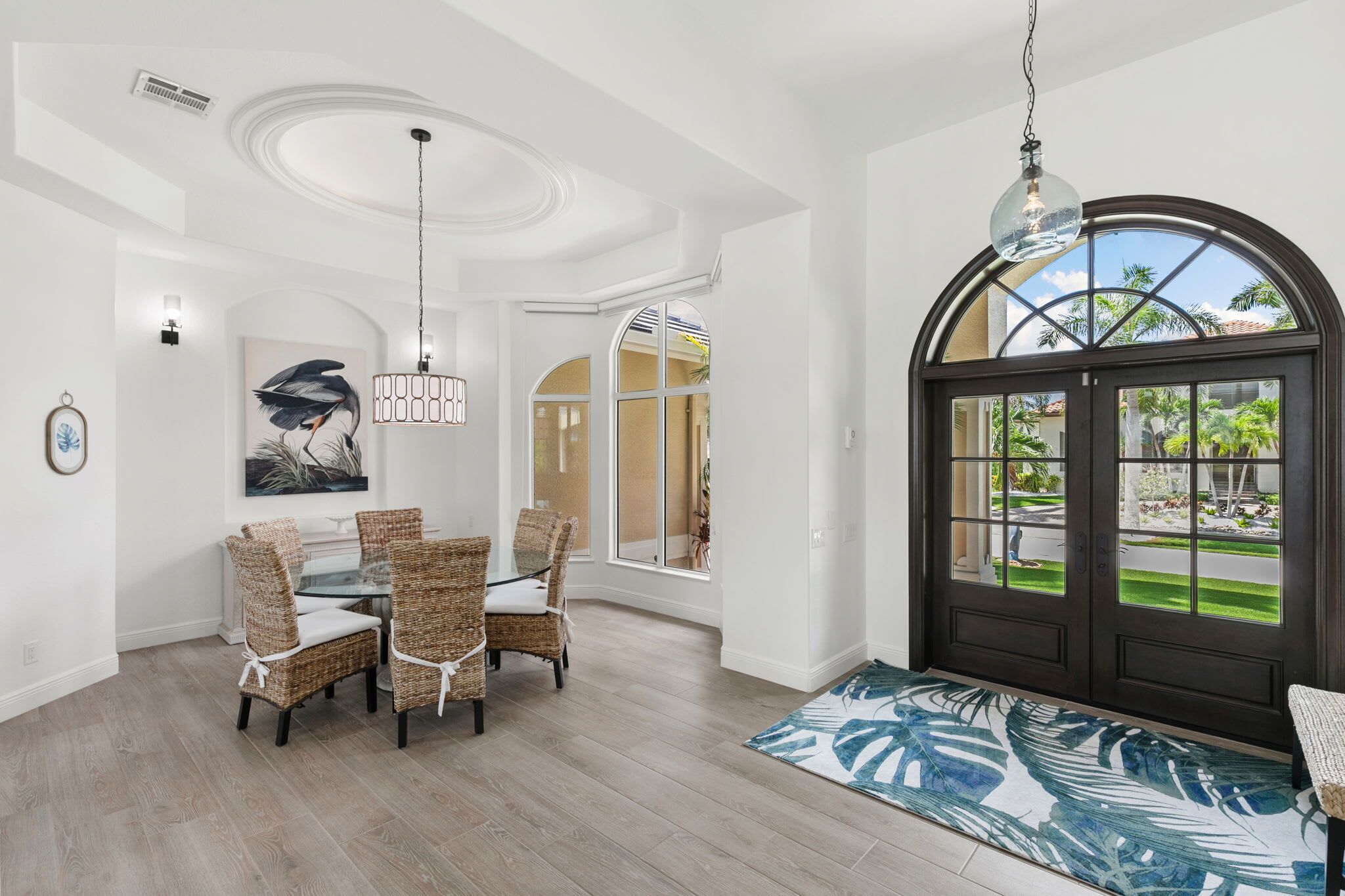 A spacious dining area with wicker chairs and a glass table, a large arched doorway leading outside, and a ceiling with recessed lighting.