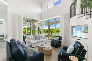 A spacious living room with a large window overlooking a pool and greenery. There are multiple seating areas with sofas and a coffee table. - Waterfront Marco Island Home w/ Pool, Spa & Kayaks (Marco Island)
