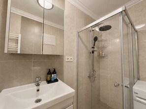 A bathroom with a glass-enclosed shower, a white sink with a mirror above it, and toiletries on the sink. - Cozy Bright 1Bd Near Bosphorus (Istanbul)