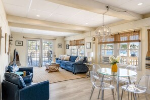 Un salón amplio con sofá azul, mesa de comedor de vidrio transparente y una araña.