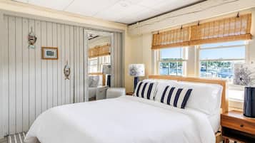 A bedroom with a large bed, a wooden headboard, a window with a view of boats, and a wall with nautical-themed decorations.