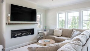 A living room with a large flat-screen TV mounted above a fireplace, a ceiling fan, and a sofa with multiple cushions. - Stay at Good Harbor Beach (Gloucester)