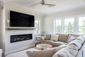 A living room with a large flat-screen TV mounted above a fireplace, a ceiling fan, and a sofa with multiple cushions. - Stay at Good Harbor Beach (Gloucester)