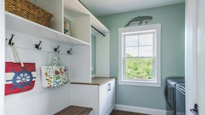 A laundry room with a wooden bench, a window with a view of greenery, and a wall-mounted basket. - Stay at Good Harbor Beach (Gloucester)