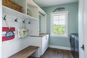 A laundry room with a wooden bench, a window with a view of greenery, and a wall-mounted basket. - Stay at Good Harbor Beach (Gloucester)