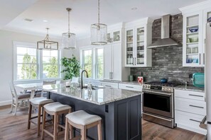 A modern kitchen with a central island, stainless steel appliances, and a stone backsplash. - Stay at Good Harbor Beach (Gloucester)