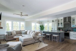 A spacious living room with a large L-shaped sofa, a coffee table, and a dining area with bar stools. The kitchen features a central island, stainless steel appliances, and a stone backsplash. - Stay at Good Harbor Beach (Gloucester)