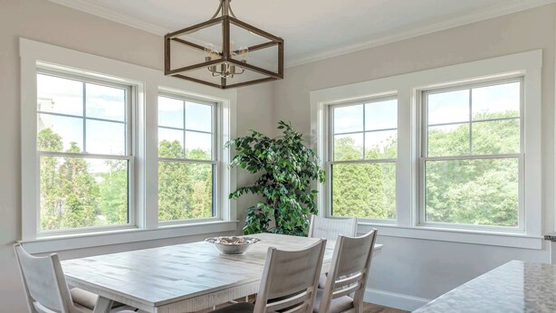 A dining area with a wooden table and chairs, large windows, and a hanging light fixture. - Stay at Good Harbor Beach (Gloucester)