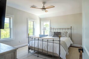 Ein Schlafzimmer mit einem Metallbettgestell, einem Deckenventilator und zwei Fenstern, die natürliches Licht hereinlassen.