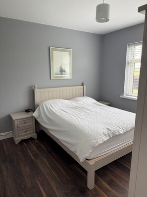 A bedroom with a bed, a nightstand, a wall-mounted picture, and a window with blinds.