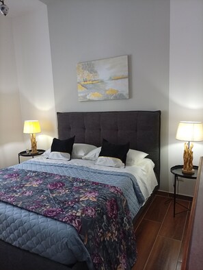 Una habitación de hotel con cama, dos mesitas de noche, un cuadro en la pared y una colcha de estampado floral.