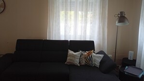 Ett vardagsrum med en mörk soffa, en lampa och ett fönster med tunna, genomskinliga gardiner.