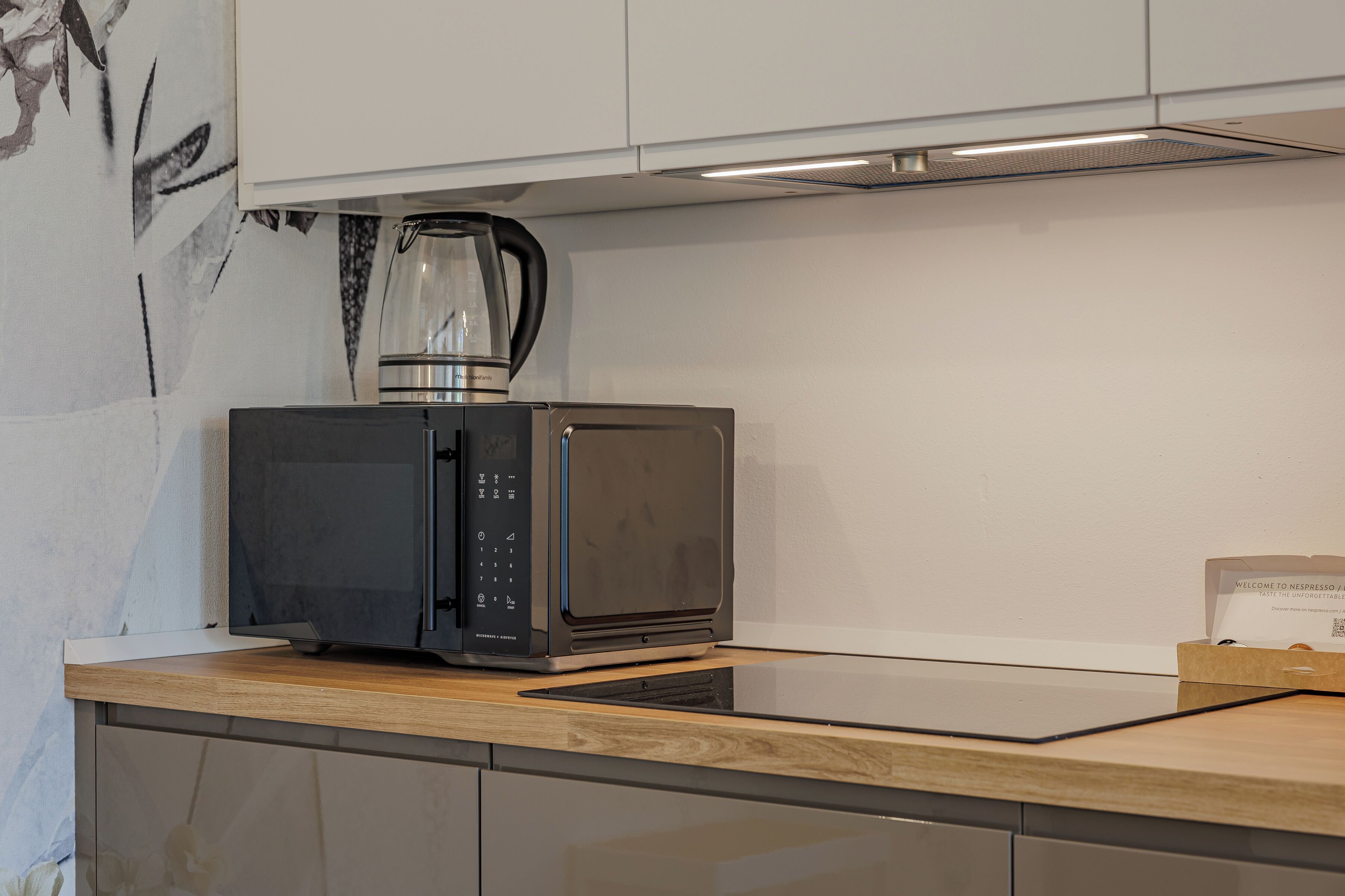 A kitchen with a microwave, a coffee maker, and a box of Nespresso capsules.
