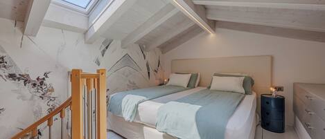 A bedroom with a skylight, a bed with multiple pillows, a bedside table, and a nightstand.