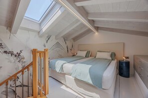 Ein Schlafzimmer mit Dachfenster, einem Bett mit vielen Kissen, einem Nachttisch und einem Beistelltisch.
