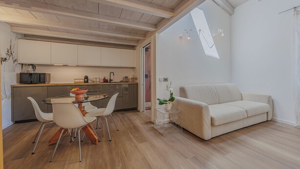 Una cocina moderna con armarios blancos, una mesa de comedor con sillas y un sofá en la sala de estar.