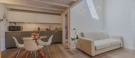 A modern kitchen with white cabinets, a dining table with chairs, and a sofa in a living area.