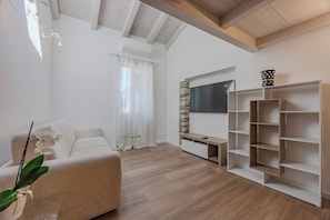 Ein modernes Wohnzimmer mit einer Couch, einem an einer Steinwand montierten Fernseher und einem hölzernen Bücherregal.