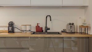 Una cocina con un lavamanos, una cafetera, un recipiente rojo y un tostador.